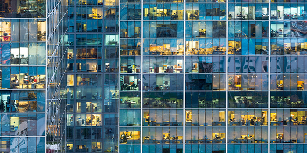 Exterior view of a modern office building with illuminated windows revealing various workspaces.